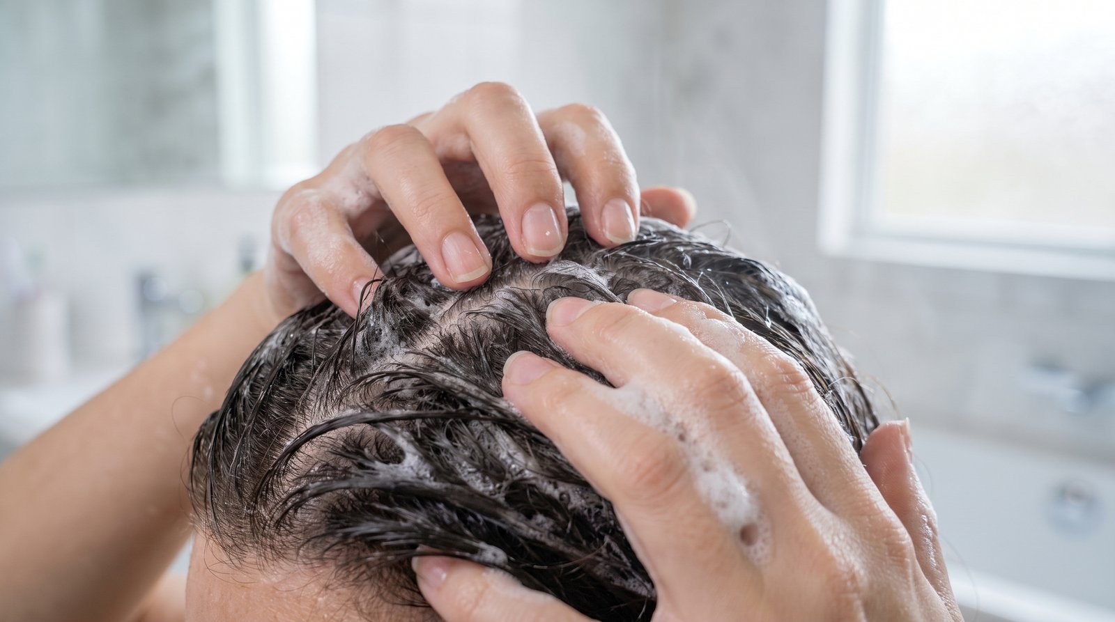 Cận cảnh đầu ngón tay xoay tròn trên da đầu qua lớp bọt dầu gội, móng tay cắt gọn